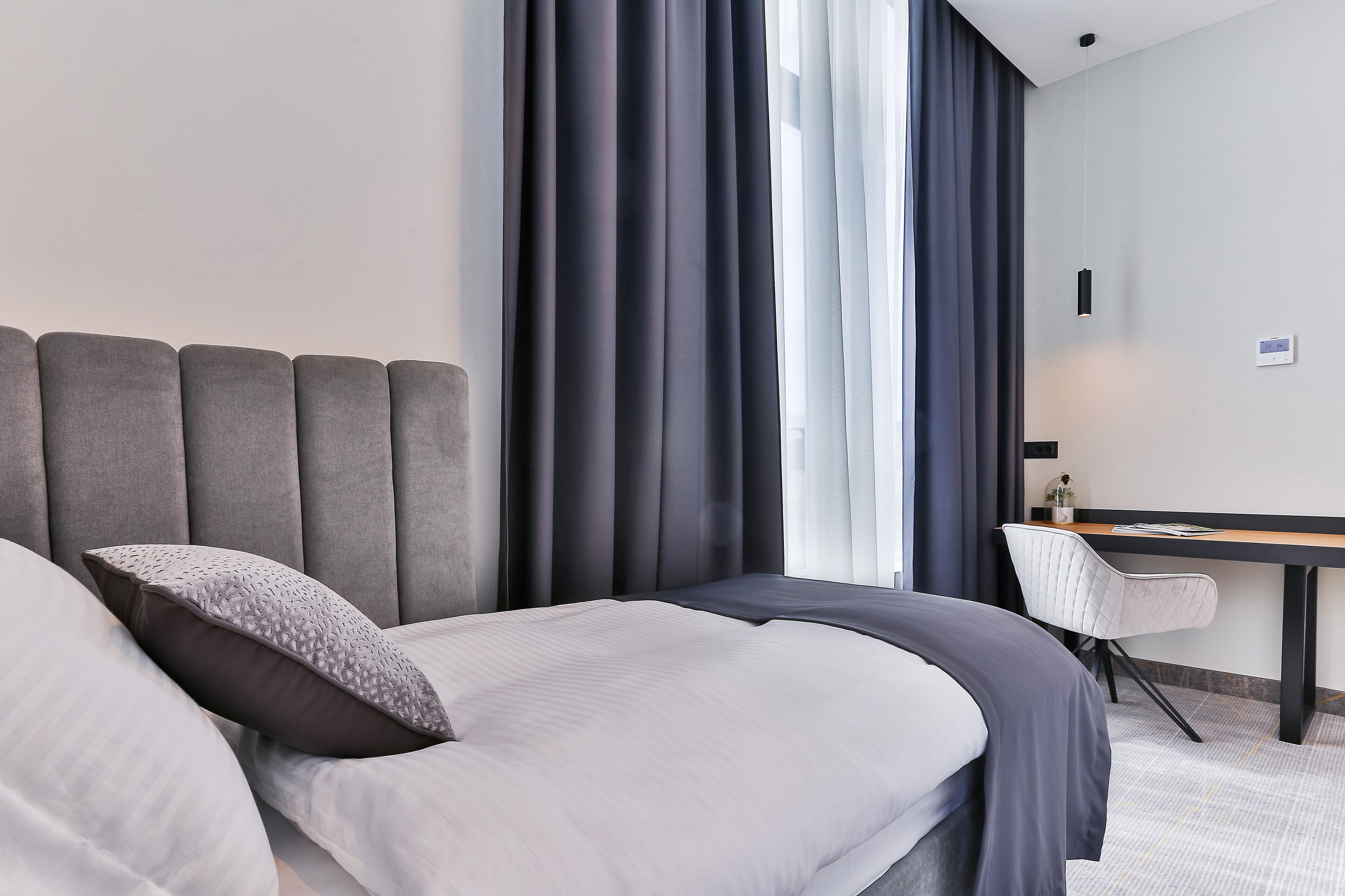 A modern hotel room with a large bed, a desk, and a chair.