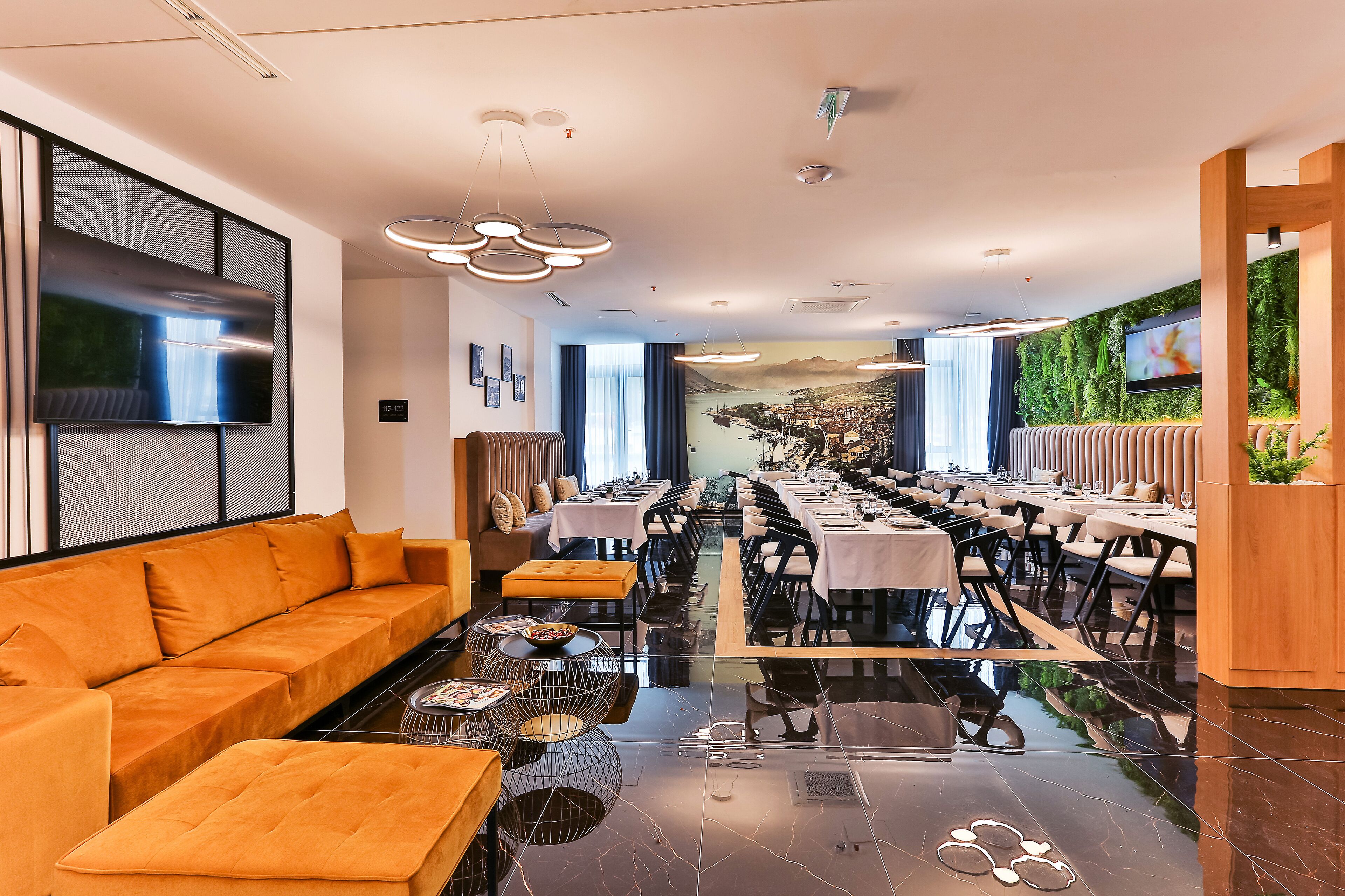 A modern dining area with a long table, orange sofa, and a mural on the wall.