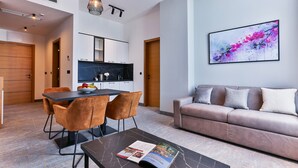 A modern living room with a sofa, a dining table with chairs, a coffee table with a magazine, and a kitchen area with cabinets and a countertop. - Hotel Boka (Radanovici)