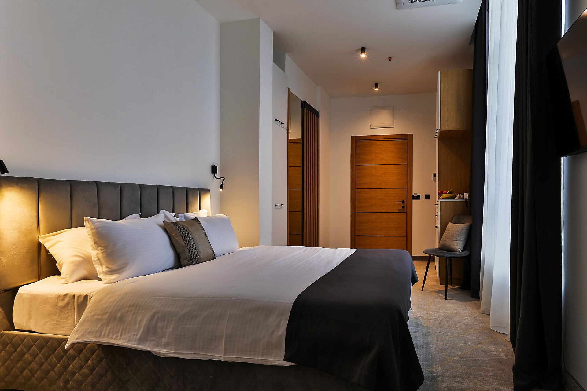 A modern hotel room with a large bed, a bedside table, and a wardrobe.