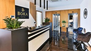 A modern hotel reception area with a black reception desk, a wooden panel wall, and a staircase leading to the upper floor. - Hotel Boka (Radanovici)