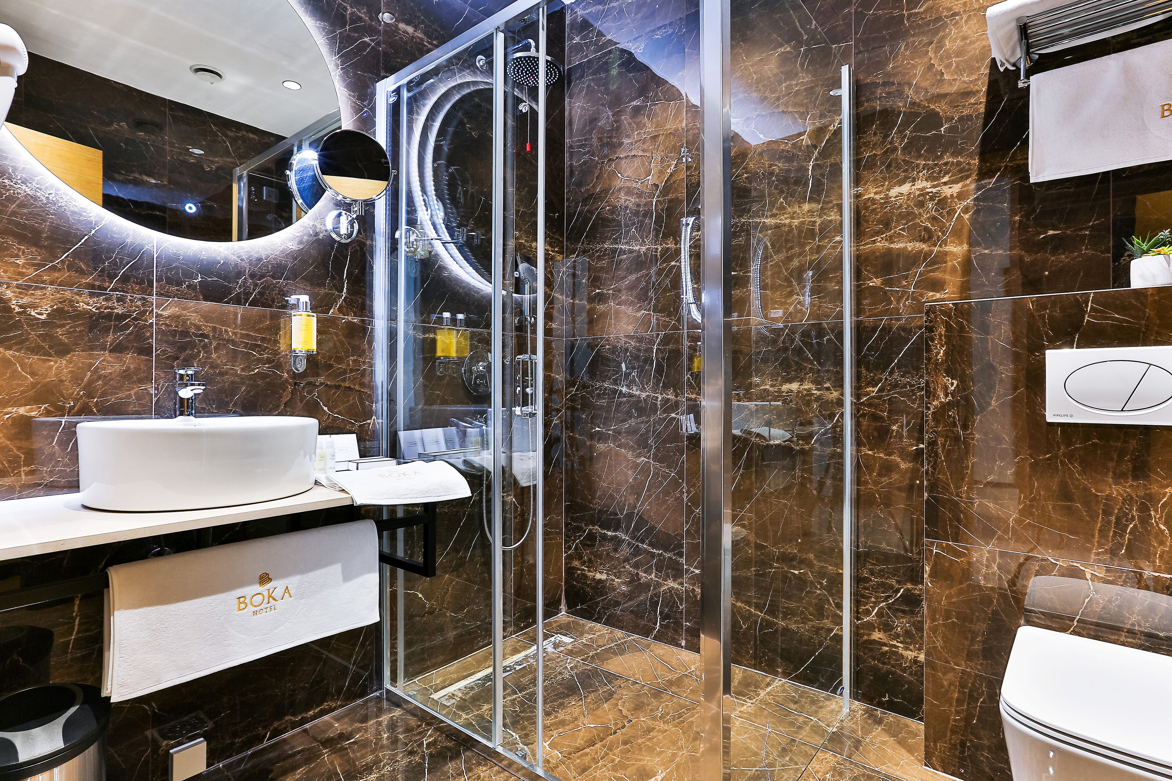 Un baño moderno con ducha envuelta en vidrio, un lavamanos blanco y una pared con azulejos de mármol.
