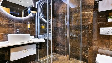 Un baño moderno con ducha envuelta en vidrio, un lavamanos blanco y una pared con azulejos de mármol.