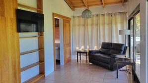Amplia sala de estar con techo alto, un sofá de cuero, un televisor montado en la pared y un ventanal con cortinas.