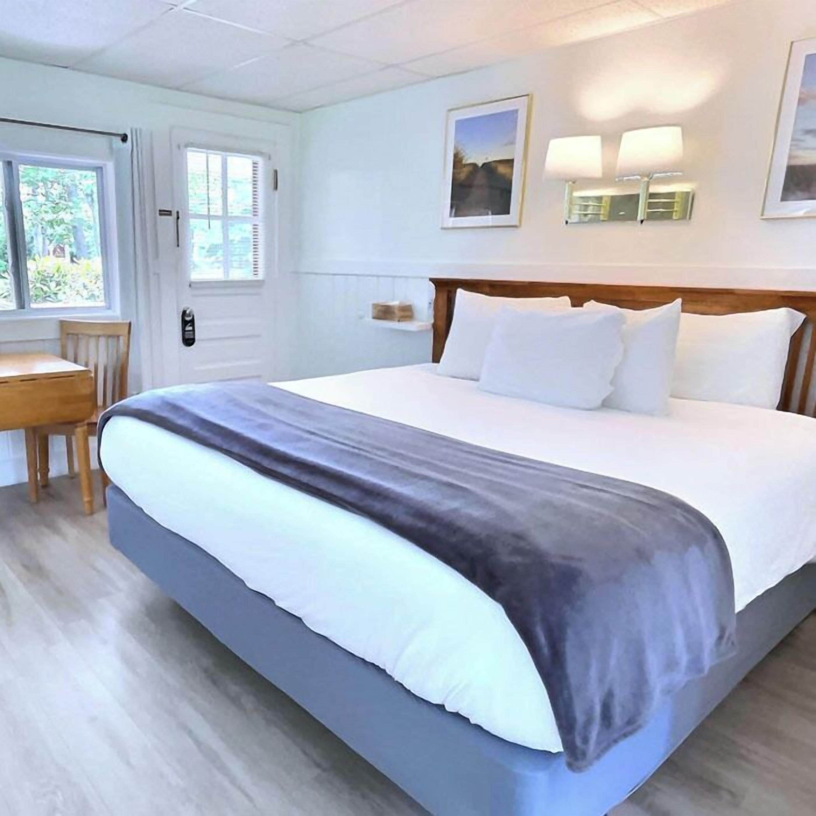 Quarto de hotel com uma cama, uma escrivaninha e duas luminárias fixadas na parede.