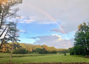 A grassy field with a rainbow, trees, and a cloudy sky. - Kennebunkport Motor Lodge (Kennebunkport)