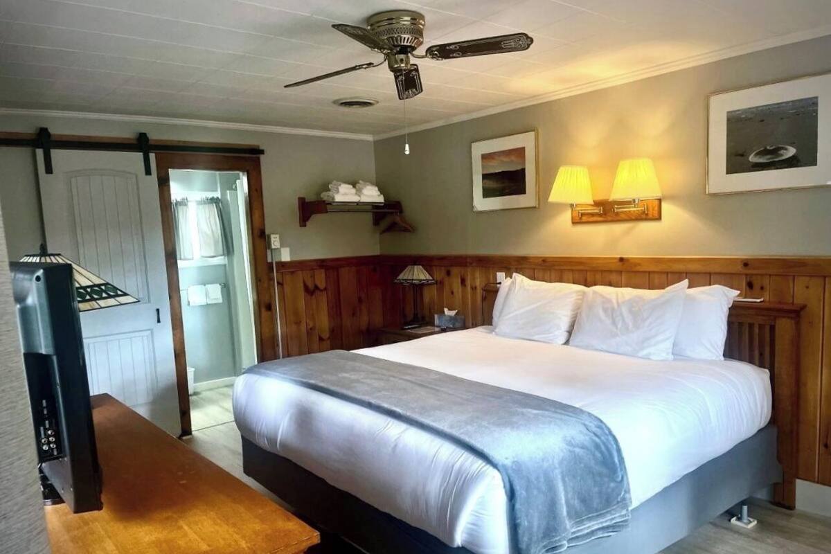 Een hotelkamer met een bed, nachtlampjes, een plafondventilator, een houten hoofdeinde en een houten bureau.