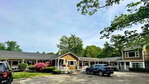 A motel with a central building and two side wings, featuring a covered parking area and lush greenery. - Kennebunkport Motor Lodge (Kennebunkport)
