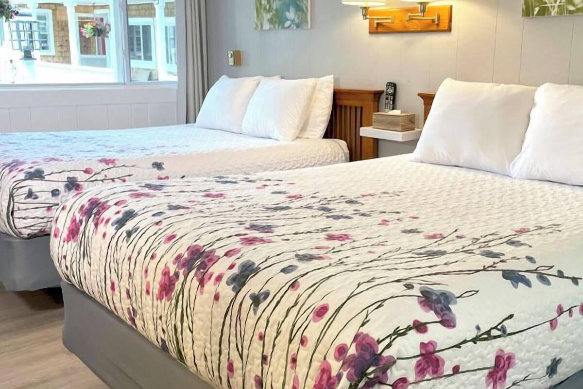 Een hotelkamer met twee bedden, een raam met gordijnen, een wandlamp en een schilderij.