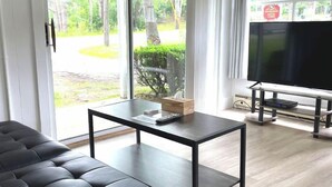 A modern living room with a black leather sofa, a glass coffee table, and a flat-screen TV on a stand. - Kennebunkport Motor Lodge (Kennebunkport)