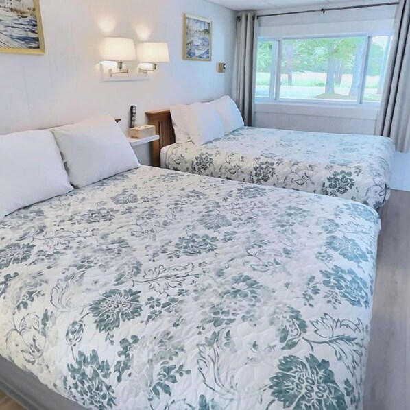 Une chambre d’hôtel avec deux lits, une table de chevet, une lampe, un tableau et une fenêtre avec des rideaux.