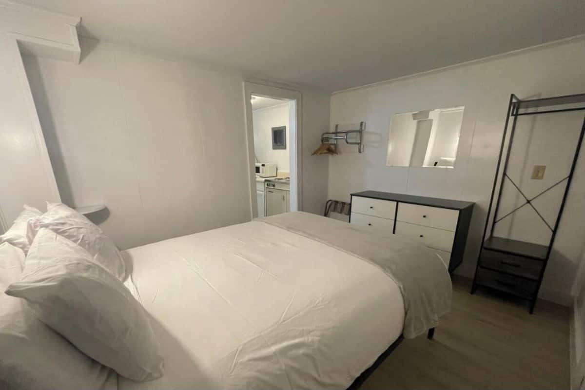 Een slaapkamer met een bed, een dressoir, een spiegel en een kast.