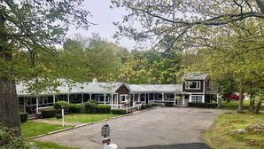 A row of two-story buildings with a covered walkway, surrounded by greenery and trees. - Kennebunkport Motor Lodge (Kennebunkport)