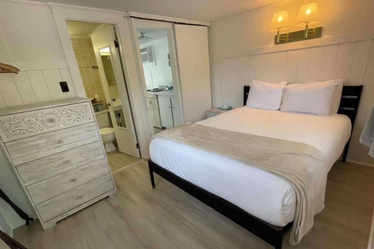 Een slaapkamer met een bed, een dressoir en een badkamer, zichtbaar door een geopende deur.
