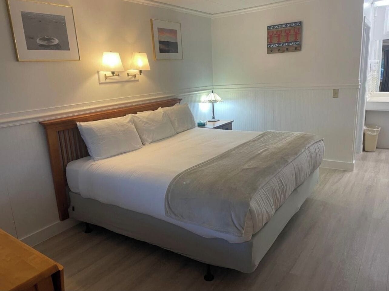 A neatly made bed in a hotel room with a wooden headboard, two wall-mounted lamps, and a framed picture above the bed.