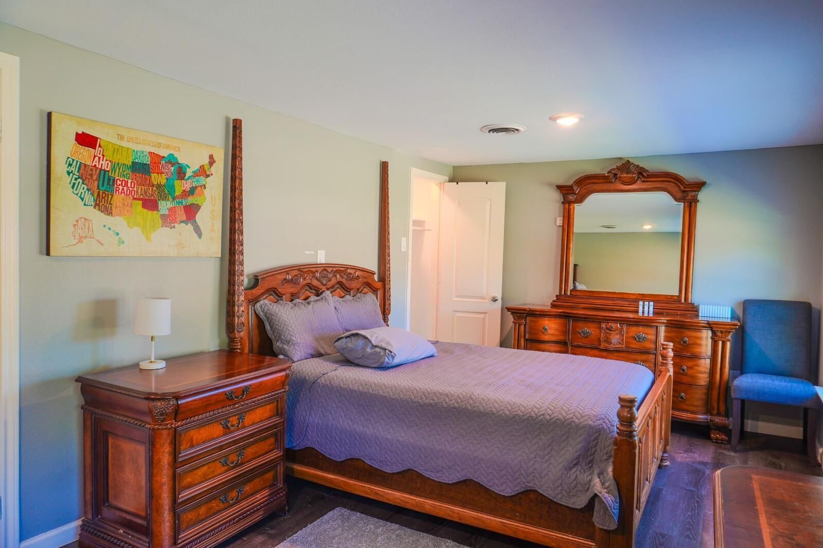 A bedroom with a wooden bed, a dresser, a mirror, and a map on the wall.