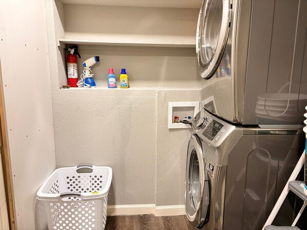 Un cuarto de lavandería con lavadora, secadora y estante con productos de limpieza.