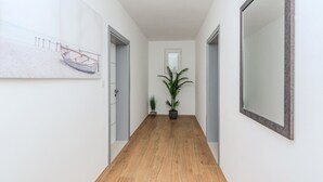 A hallway with wooden flooring, white walls, and a large mirror on the right. There is a door on the left and a window with blinds in the center. - Stunning apartment in Privlaka with WiFi (Privlaka)