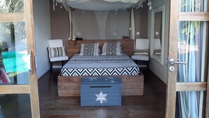 Ein Schlafzimmer mit einem Bett, Nachttischen, einem Baldachin, einem Spiegel und einem Fenster mit Blick auf Palmen.
