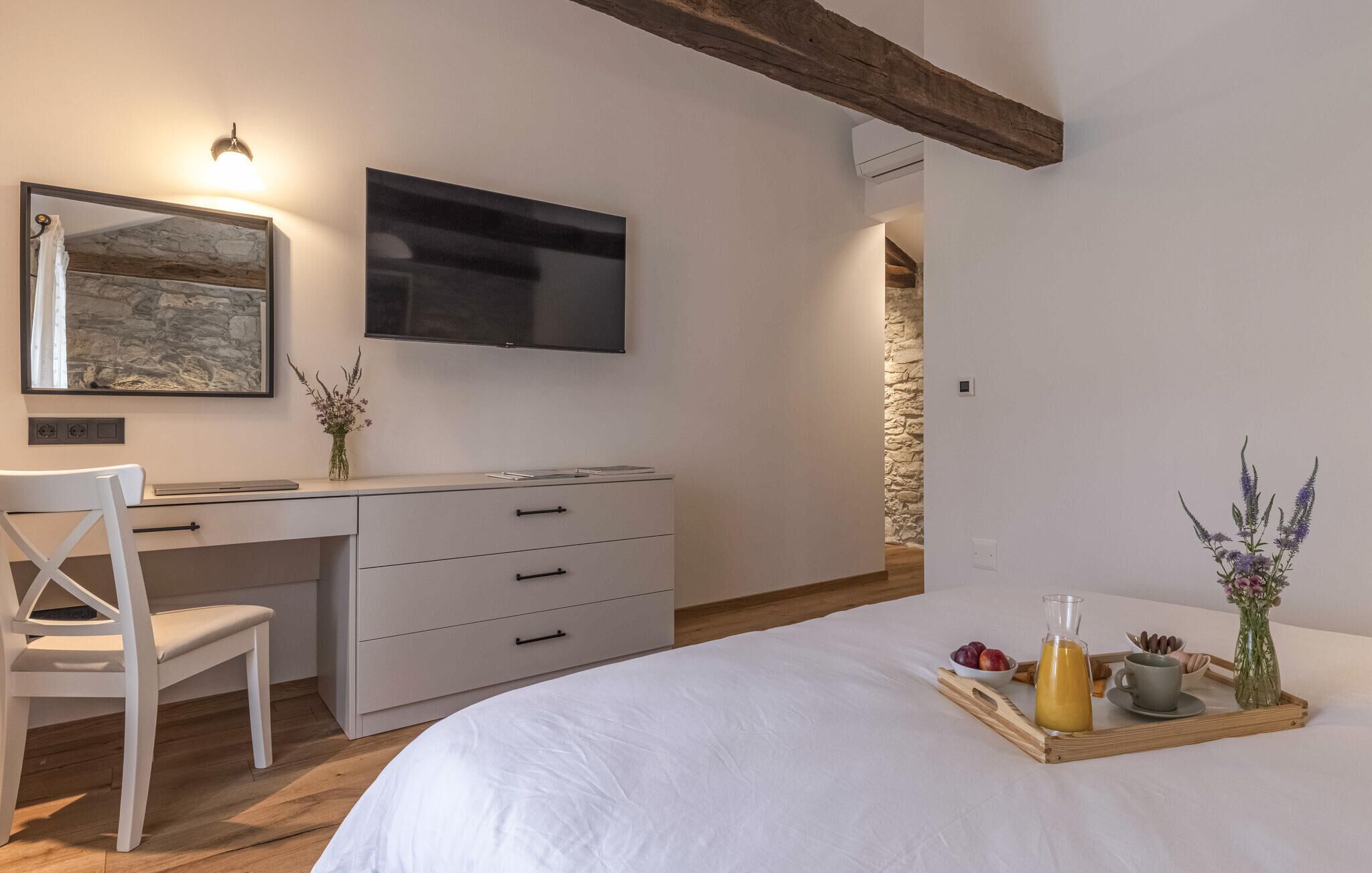 Ein Schlafzimmer mit Bett, Schreibtisch, Stuhl, Fernseher und einem Frühstückswagen mit Obst und Getränken.