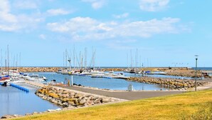 Un puerto deportivo con barcos amarrados, un rompeolas rocoso y un cielo despejado.