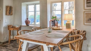 Un comedor con una mesa y sillas de madera, un florero con flores, una lámpara y una ventana que ofrece vistas al exterior.
