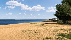 Una playa con cielo despejado y algunas nubes. Hay un árbol a la derecha y algunos barcos al fondo.