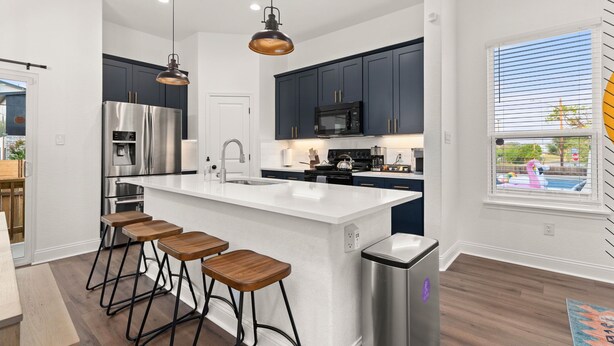 A modern kitchen with dark cabinets, stainless steel appliances, a large island with stools, and a view of a swimming pool through a window.
