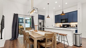 A modern kitchen with dark blue cabinets, stainless steel appliances, and a wooden dining table with bar stools.