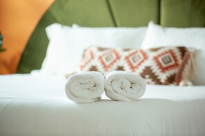 A bed with white linens and two rolled towels placed on it.
