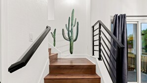 A staircase with wooden steps and a black railing, leading to a glass door with a view of greenery outside.