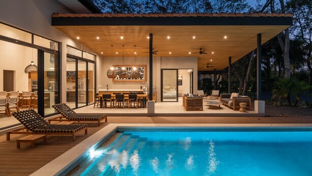 A modern outdoor pool area with lounge chairs, a dining area, and a covered patio.