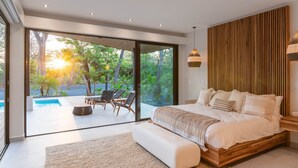 A modern bedroom with a large bed, a view of a swimming pool, and a wooden wall.