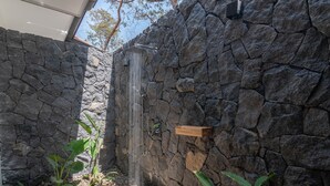 A stone wall with a built-in shower, surrounded by plants and a wooden shelf.