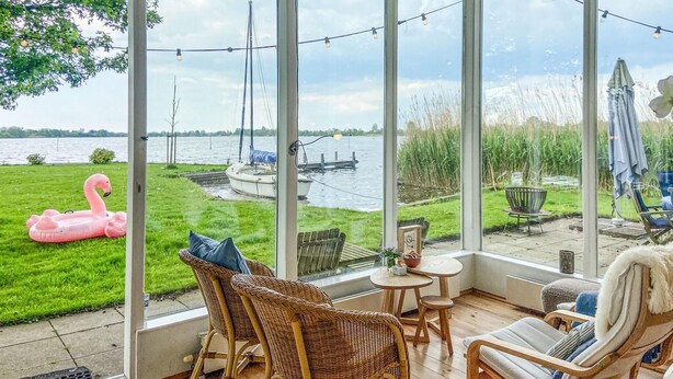En inglasad uteplats med flätade stolar, ett litet bord och utsikt över en sjö med båtar och en rosa flamingo.
