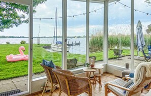 A covered patio with wicker chairs, a small table, and a view of a lake with boats and a pink flamingo. - 2 bedroom beautiful home in Reeuwijk (Reeuwijk)