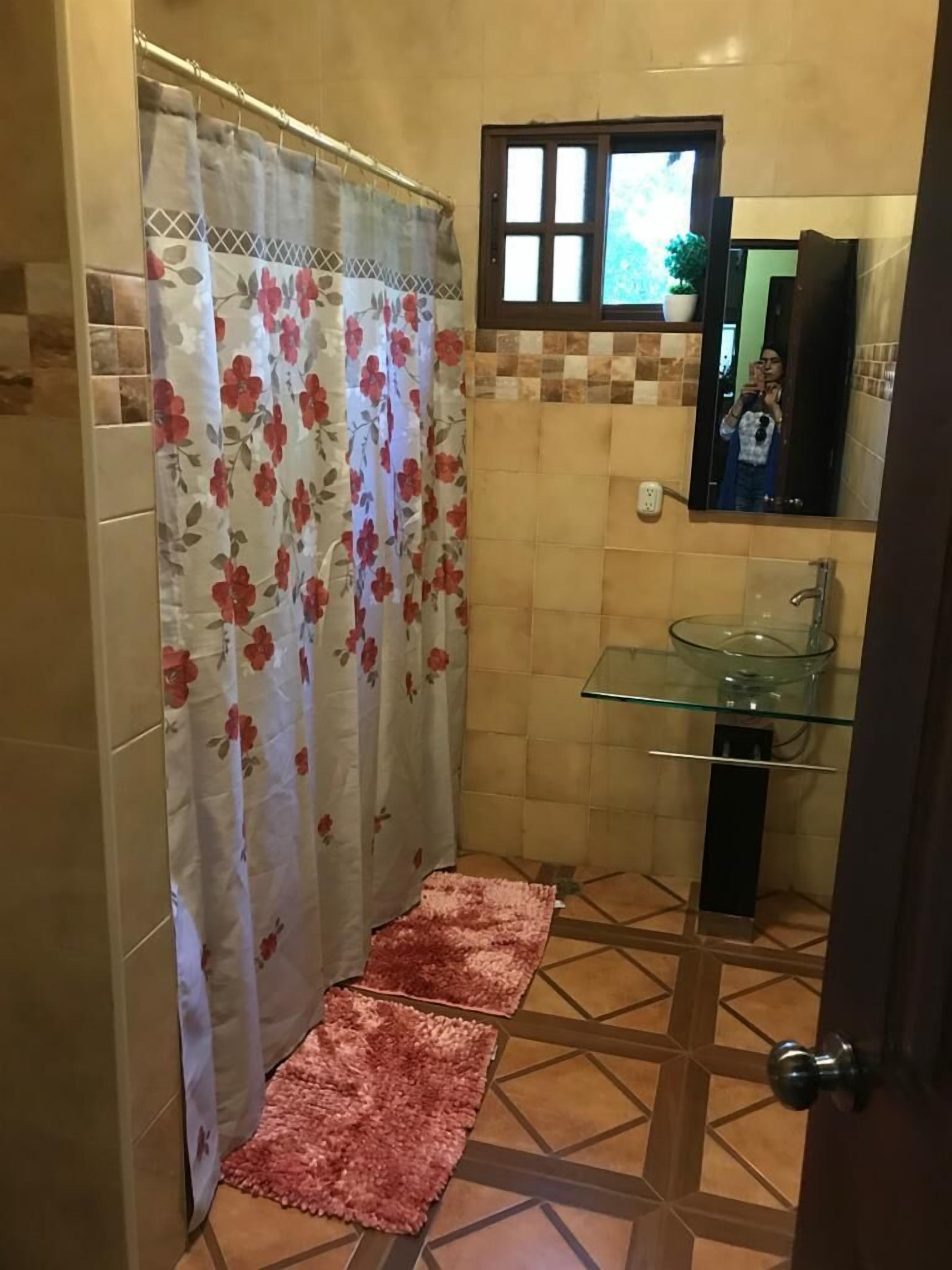 Uma casa de banho com lavatório de vidro, separador de chuveiro com padrão floral e chão em mosaico com design geométrico.