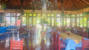 A spacious dining area with high ceilings, wooden beams, and large windows. Tables are set with chairs, and a chandelier hangs from the ceiling. - Brisas de los Alpes (Jarabacoa)