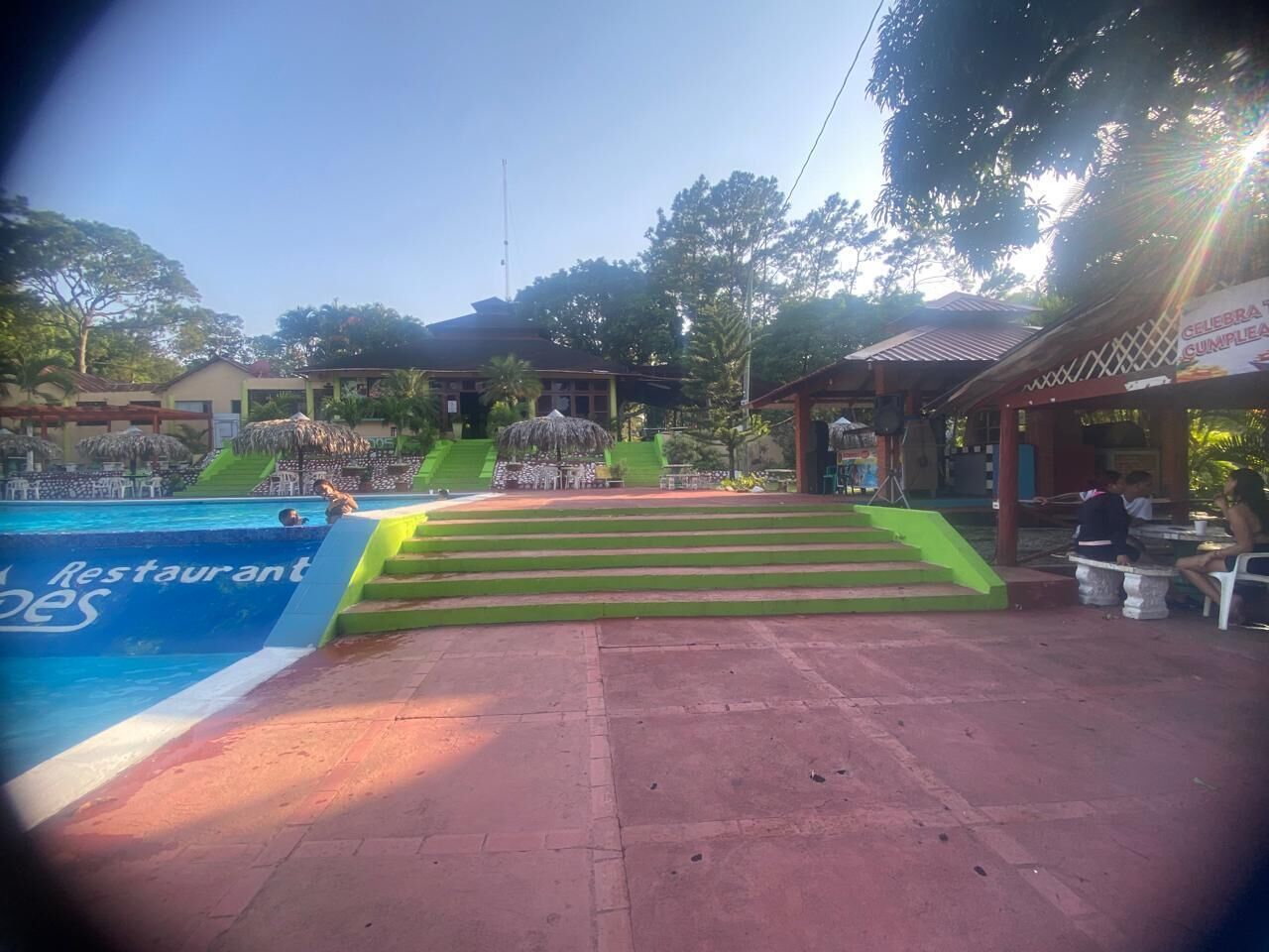 A swimming pool with steps leading to a covered area, a restaurant sign, and outdoor seating.