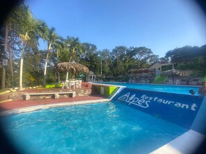 Una piscina con un letrero de restaurante, rodeada de palmeras y un pabellón.