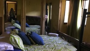 A room with two beds, each with patterned bedding and pillows. There is a wooden headboard and a green area rug. A mirror is visible on the wall, and a door leads to another room. - Brisas de los Alpes (Jarabacoa)