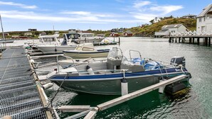 A marina with several boats docked, a wooden pier, and houses in the background.