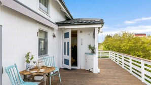 A wooden deck with a white railing, a table with chairs, and a door leading to an interior space.