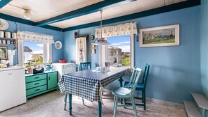 A room with a checkered tablecloth, teal chairs, a green cabinet, and a painting on the wall.