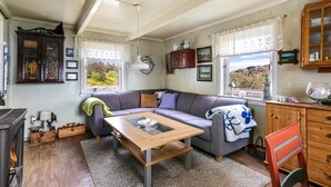 A cozy living room with a fireplace, a sofa, a wooden coffee table, and a view of the outdoors through the windows.