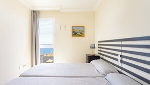 Une chambre d’hôtel avec deux lits, un tableau au mur et une vue sur la mer par la fenêtre.