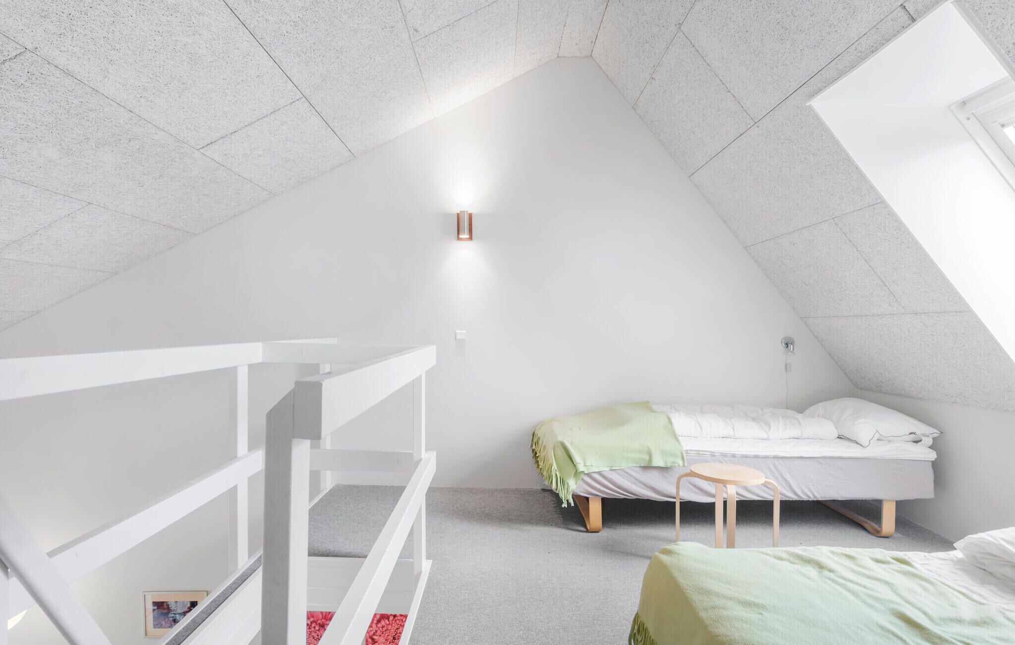 Une chambre à coucher moderne et minimaliste, avec un plafond en pente, un lit simple, un petit tabouret et une balustrade blanche.