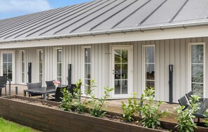 Un bâtiment doté d’un toit en métal gris, de murs extérieurs blancs et d’un patio couvert aménagé avec des meubles d’extérieur et des jardinières.