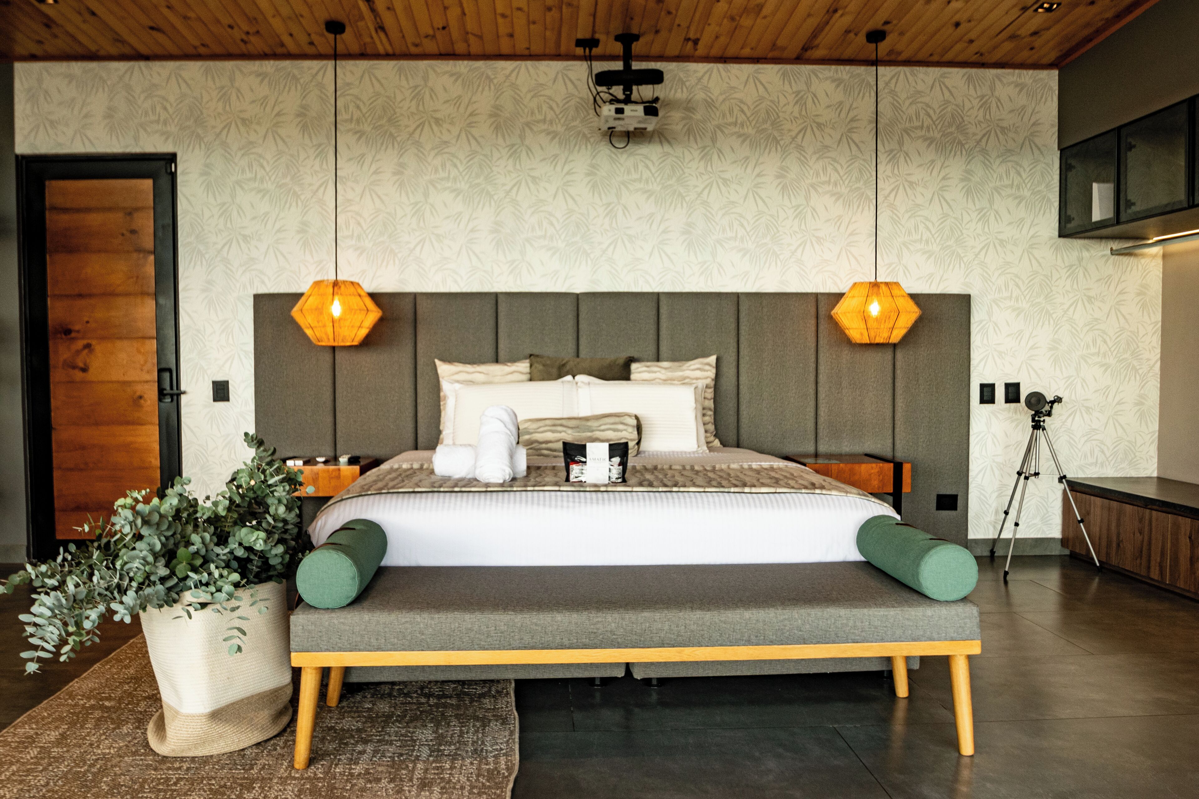 A modern bedroom with a large bed, wooden headboard, and two pendant lights.