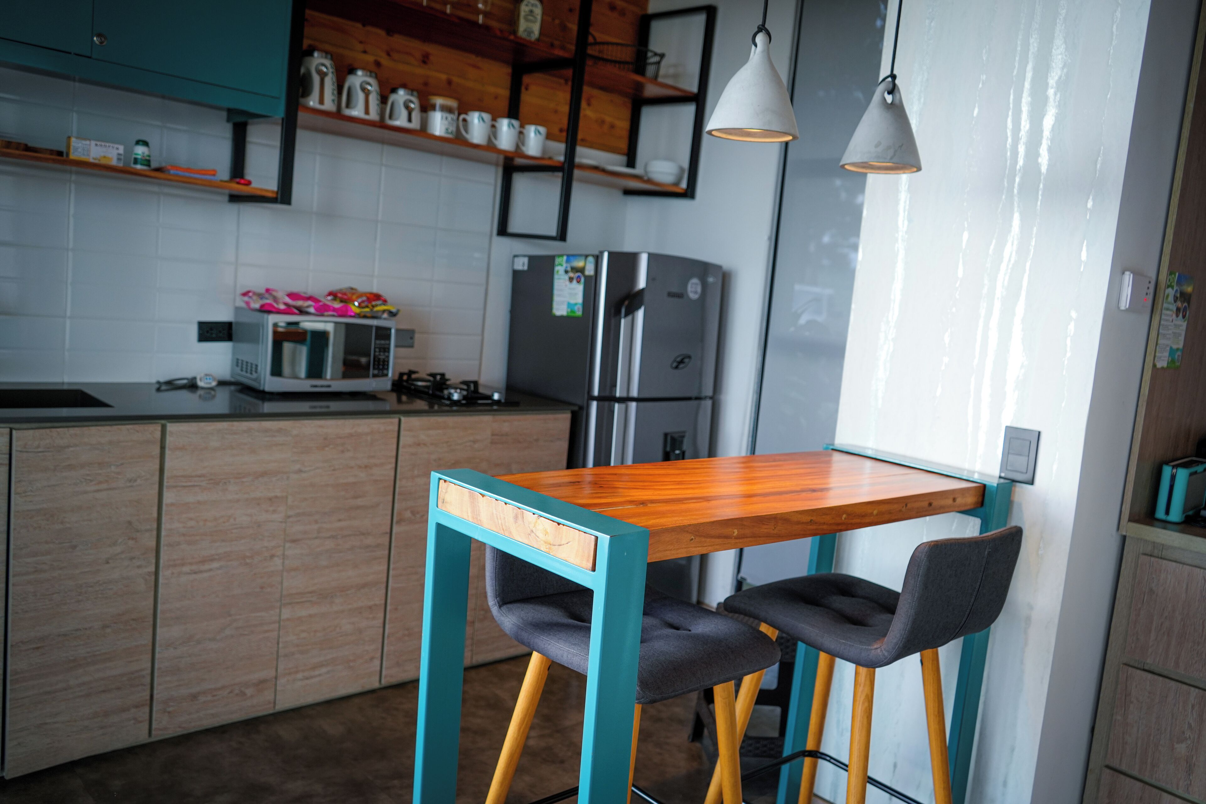 A modern kitchen with wooden cabinets, a stainless steel refrigerator, a microwave, and a wooden table with two chairs.